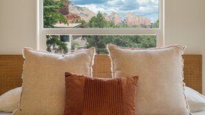 Una cama con tres almohadas y vistas a las montañas a través de una ventana.