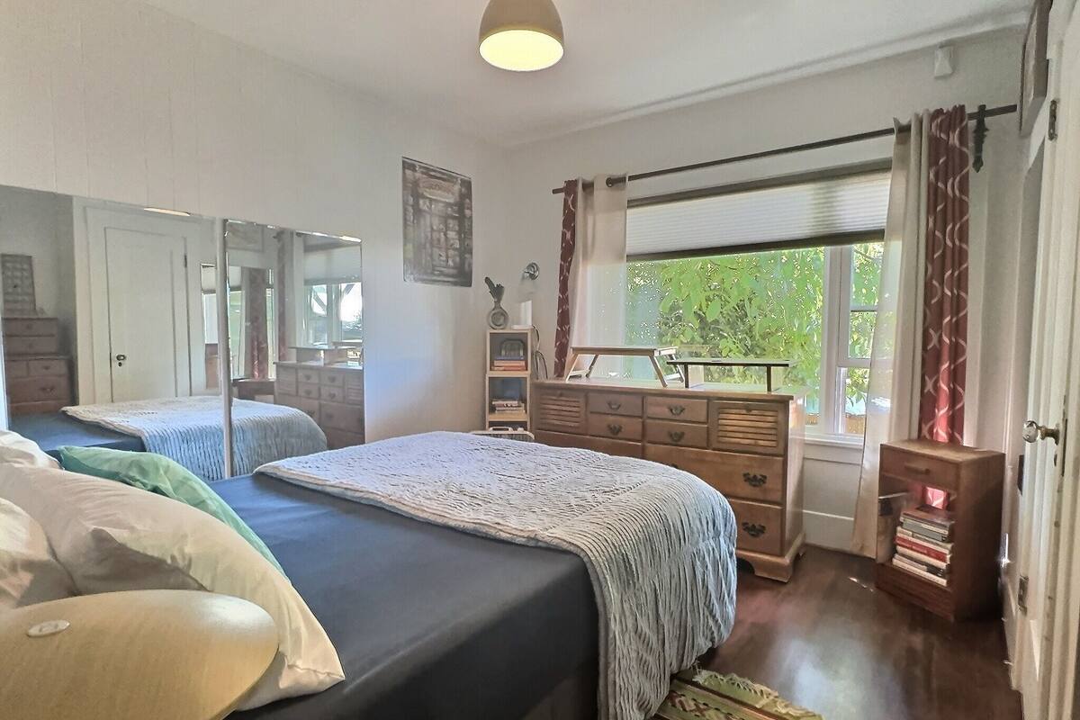Quarto com duas camas, uma cômoda, um espelho e uma janela com cortinas.