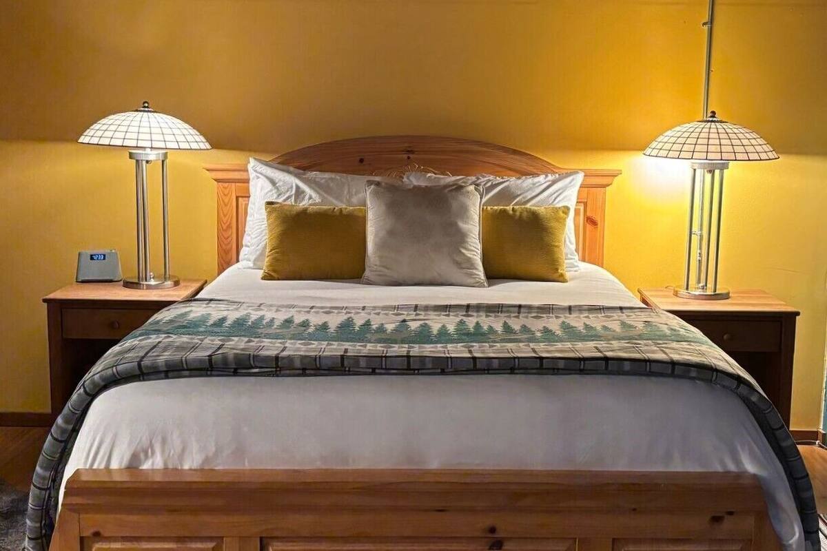 Uma cama com cabeceira de madeira, duas luminárias de cabeceira e um cobertor estampado.