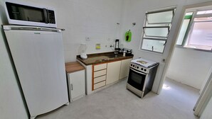 A compact kitchen with a refrigerator, microwave, stove, and a small countertop. - Renovated apartment, just 250m from the sea, fast Wi-Fi, close to the Aquarium, for 4 people (Guarujá)