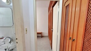 A hallway with a bathroom on the left, wooden doors on the right, and a bench in the distance. - Renovated apartment, just 250m from the sea, fast Wi-Fi, close to the Aquarium, for 4 people (Guarujá)