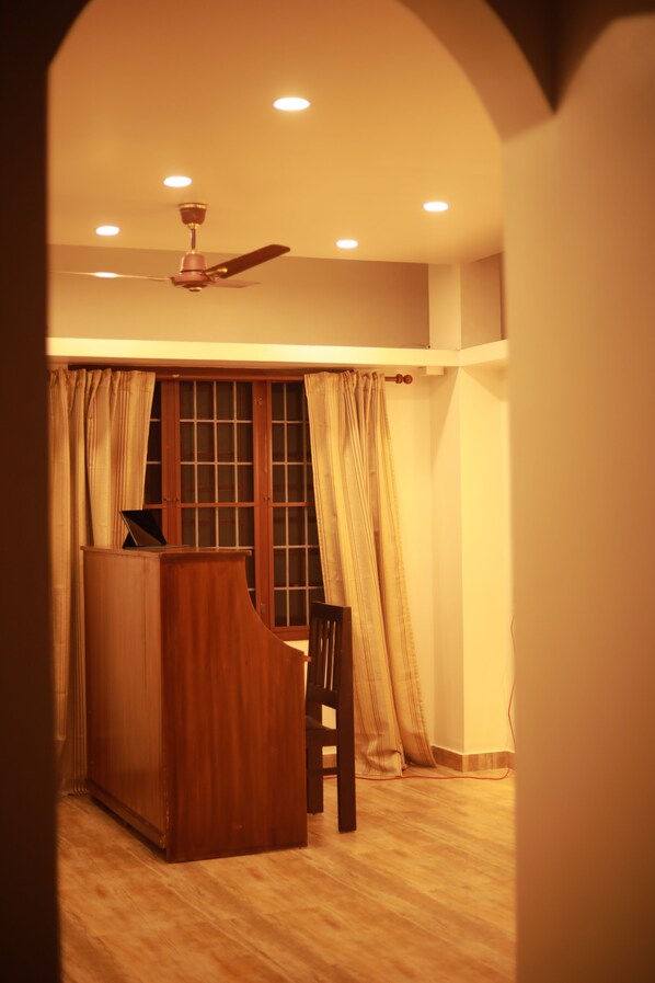 A room with a wooden desk, a chair, a ceiling fan, and a window with curtains. - Fort Verdant Homestay (Kochi)