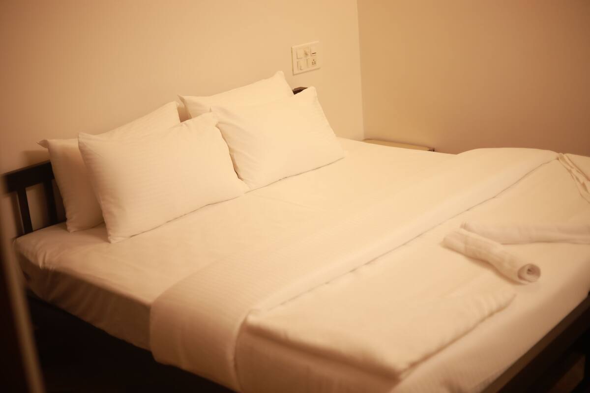 Een net opgemaakt bed met witte lakens en kussens, een houten hoofdbord en een stopcontact aan de muur.