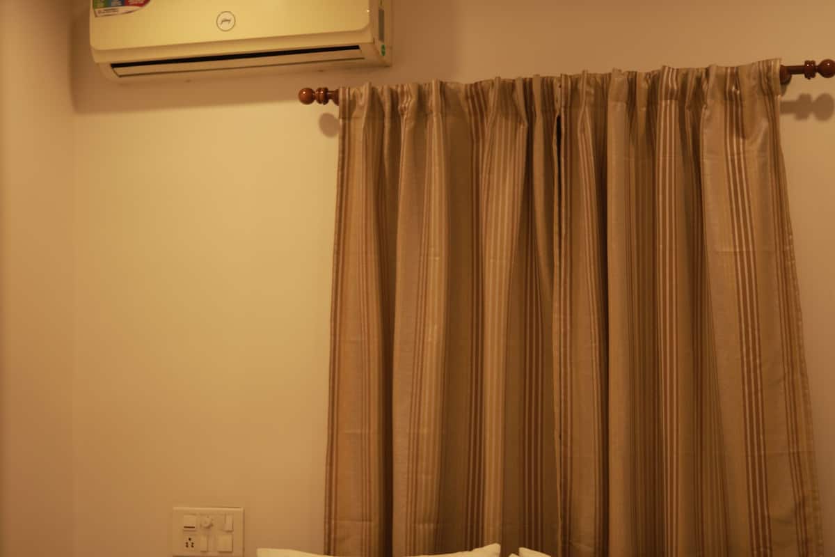 Een hotelkamer met een bed, kussens, een plafondventilator, een airconditioning en gordijnen.