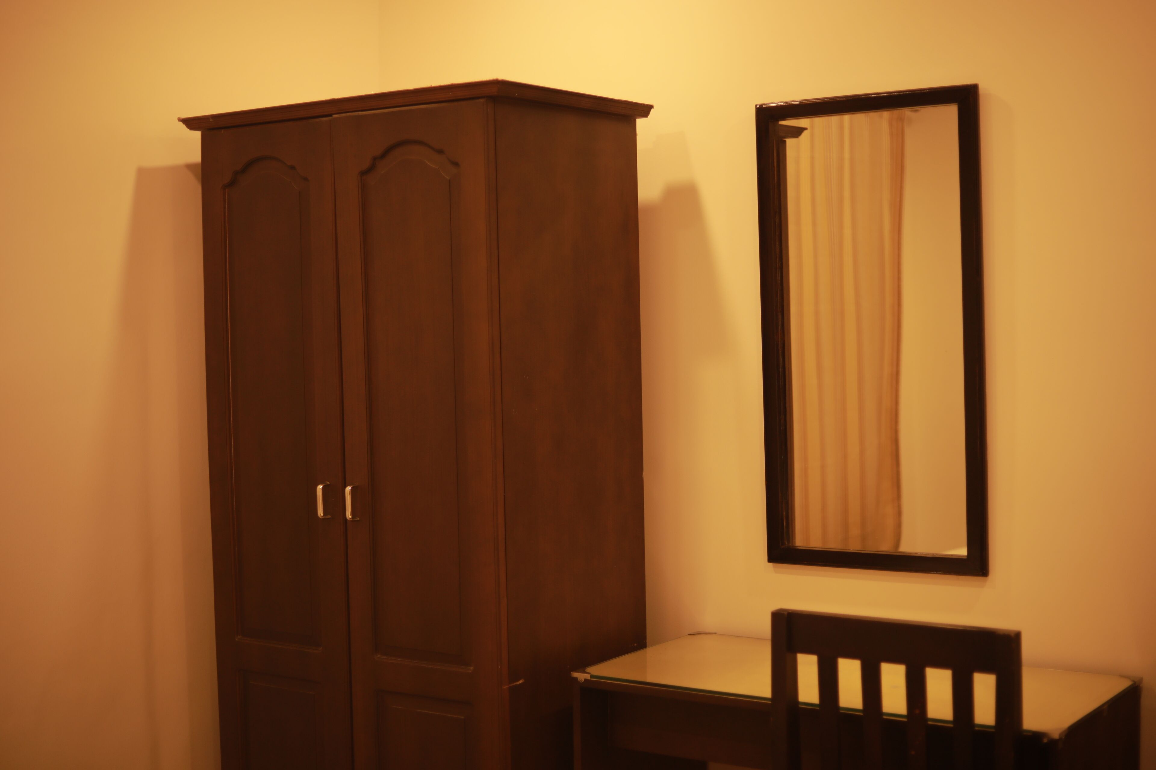 A room with a wooden wardrobe, a mirror, and a chair.