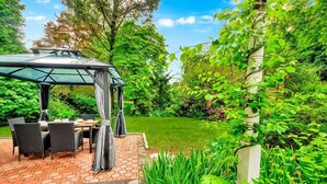 A patio with a glass gazebo, outdoor furniture, and a well-maintained garden. - Modern Comfort in the Heart of NYC (Yonkers)