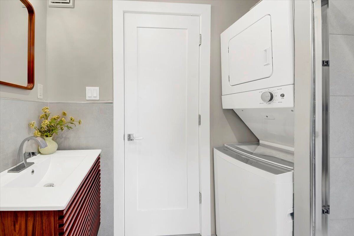 A bathroom with a white sink, a mirror, a door, and a washing machine.