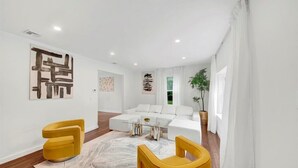 A modern living room with a white sectional sofa, two yellow chairs, a glass coffee table, and abstract art on the walls. - Modern Comfort in the Heart of NYC (Yonkers)