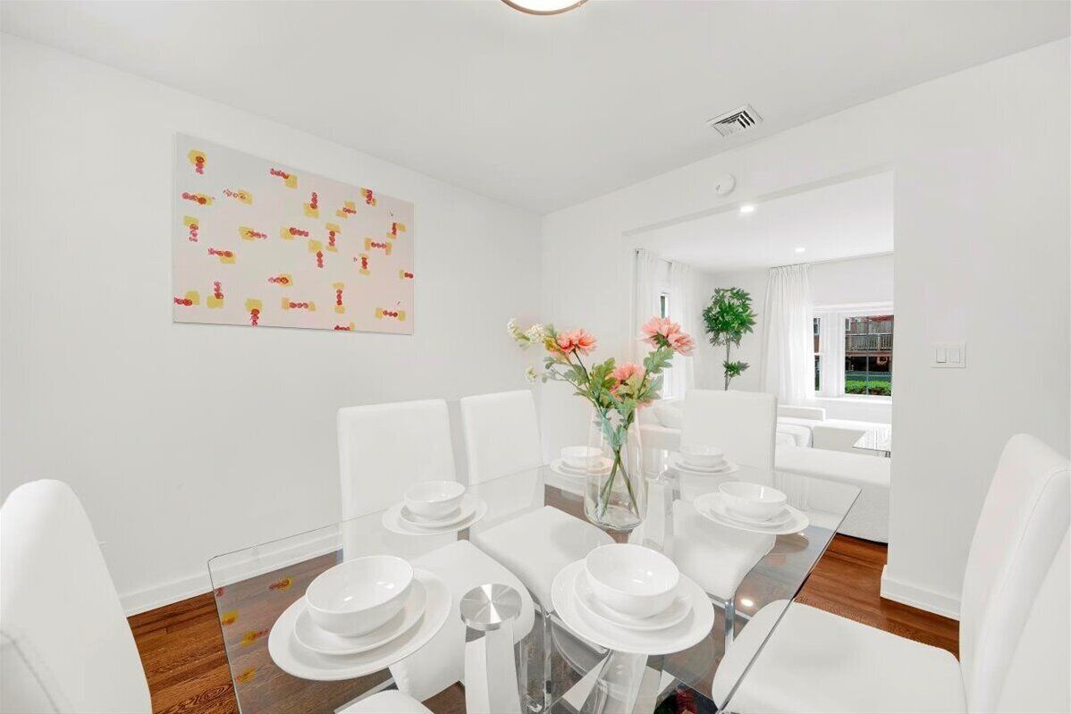 A modern dining room with a glass table, white chairs, and a vase of flowers.