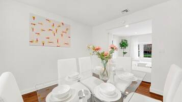A modern dining room with a glass table, white chairs, and a vase of flowers.