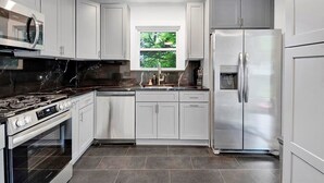 A modern kitchen with white cabinets, a stainless steel refrigerator, a built-in oven, and a microwave. - Modern Comfort in the Heart of NYC (Yonkers)