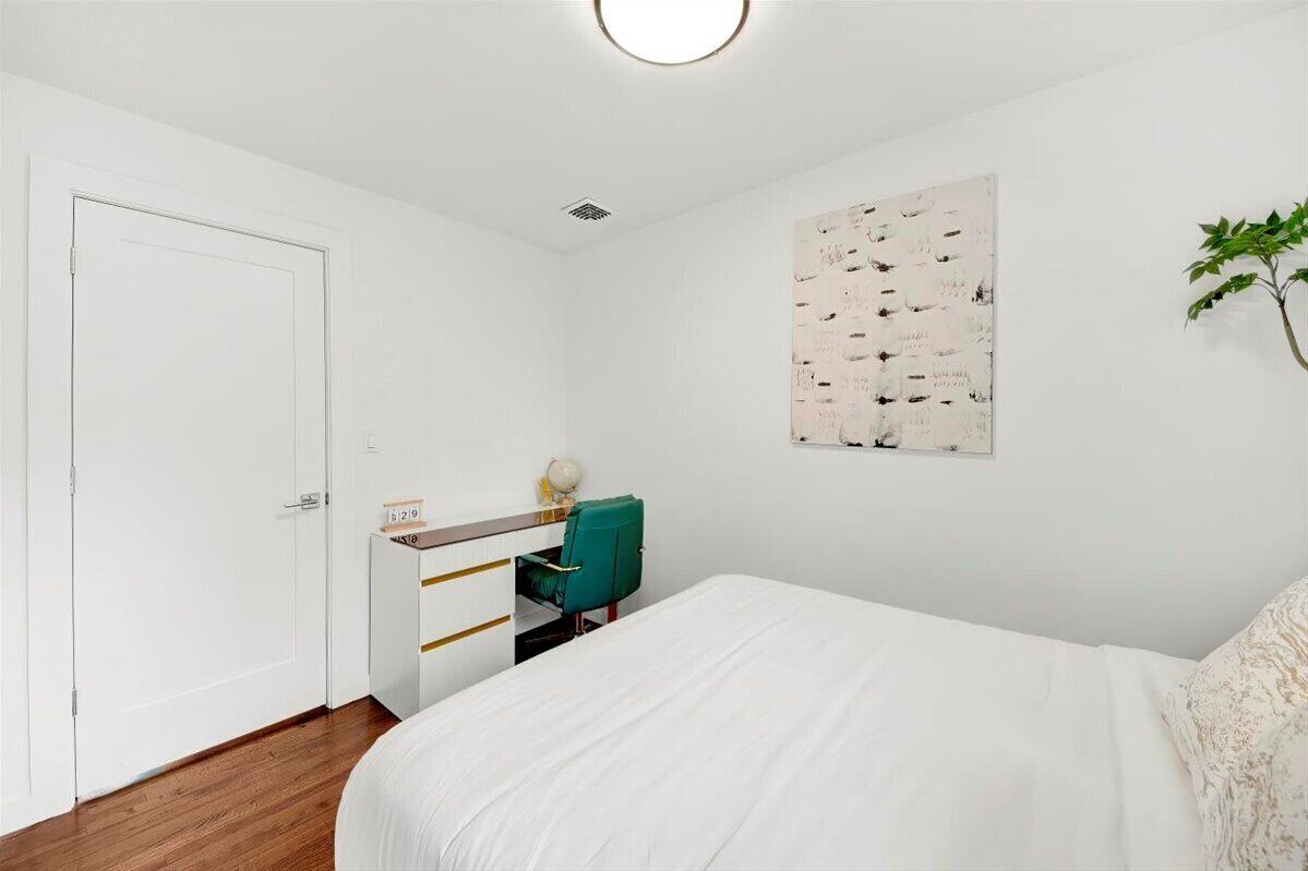 A bedroom with a bed, a desk with a chair, a wall-mounted artwork, and a door.