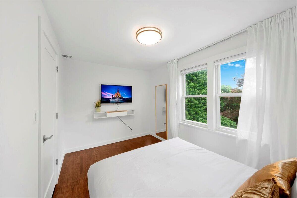Une chambre à coucher avec un lit, un téléviseur fixé au mur et une fenêtre avec des rideaux.