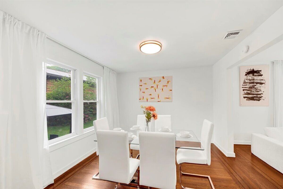 A dining area with a table set for four, white chairs, and a vase with flowers.