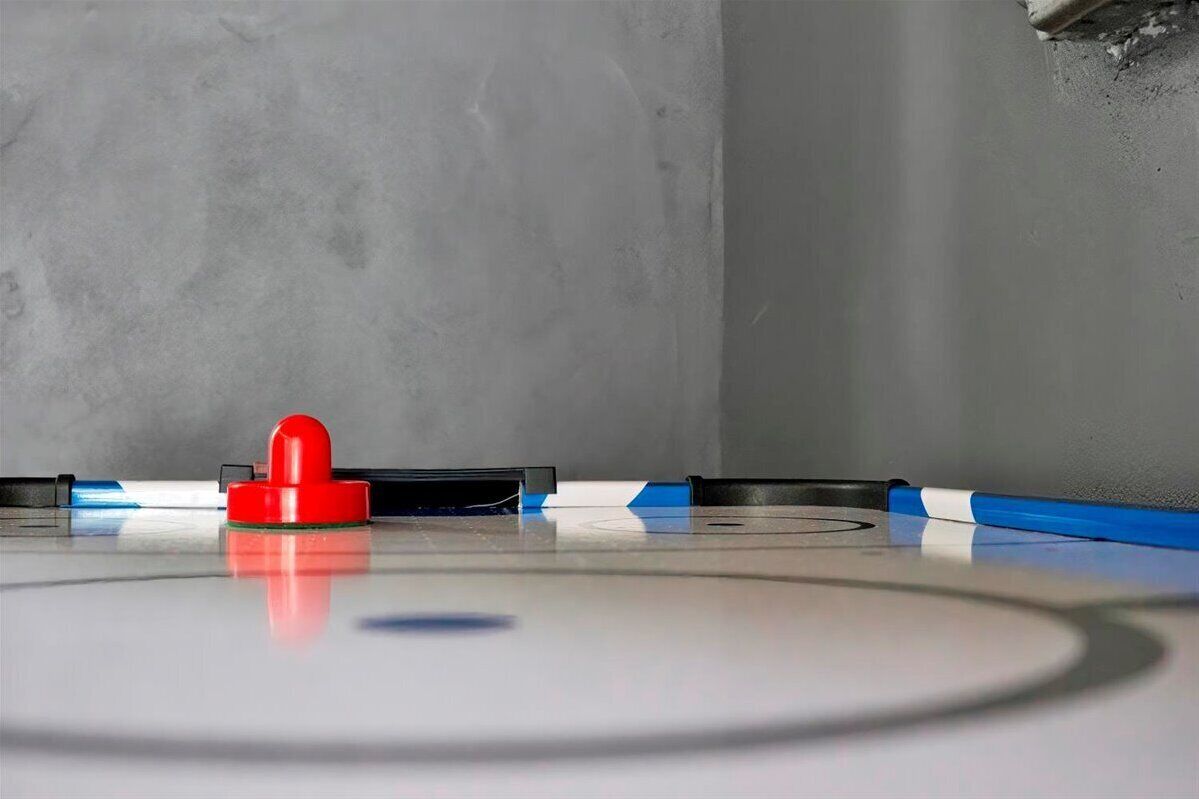 A close-up of a curling stone on a curling sheet with a red handle, reflecting on the surface.