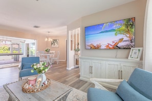 A living room with a large TV, a dining area, and a view of the outdoors.