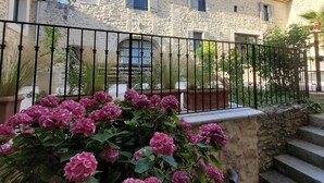 A stone building with a black wrought iron fence, potted plants, and pink flowers in the foreground. - Self-contained studio located in Mas Saint-Raphaël (Solérieux)