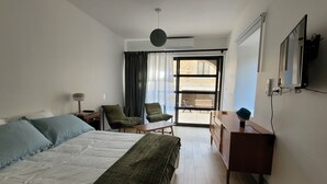 A hotel room with a bed, two chairs, a desk, a TV, and a sliding glass door to the outside. - Self-contained studio located in Mas Saint-Raphaël (Solérieux)