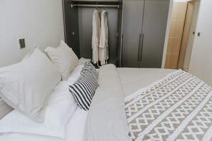 Una cama bien tendida con ropa blanca y una colcha estampada.