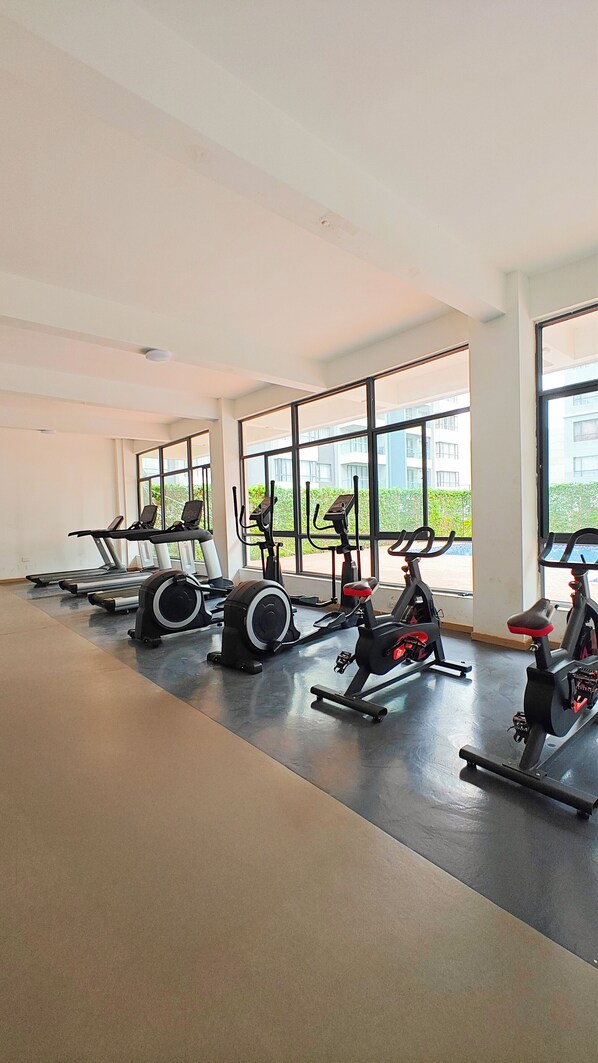 Un gimnasio con máquinas de cardio y ventanas amplias.