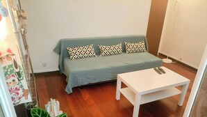 Una habitación pequeña con un sofá verde, almohadones estampados, una mesa blanca y una planta verde grande.