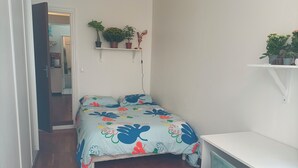 Un dormitorio pequeño y ordenado con cama, escritorio y estante con plantas.
