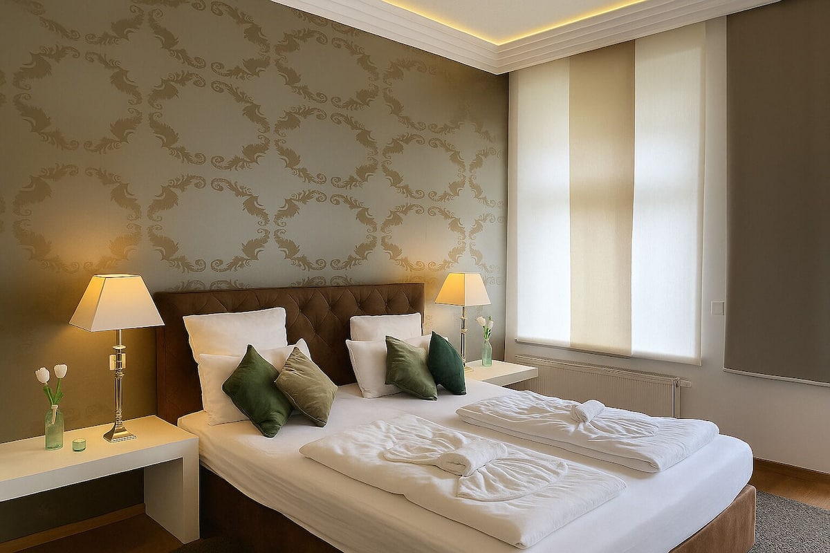 A hotel room with a large bed, two bedside tables, a nightstand, a window with blinds, and a decorative wall pattern.