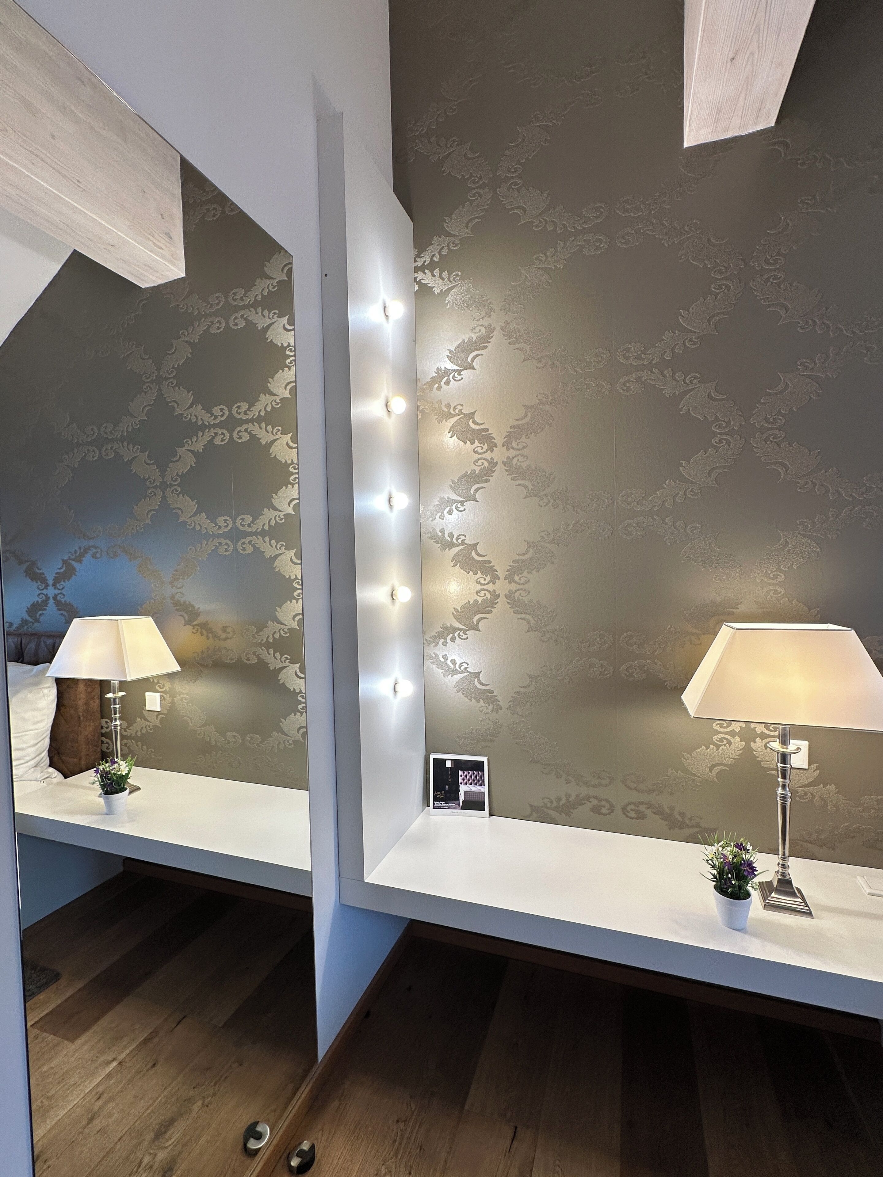 A room with a vanity mirror, two lamps, and a decorative wall with a floral pattern.