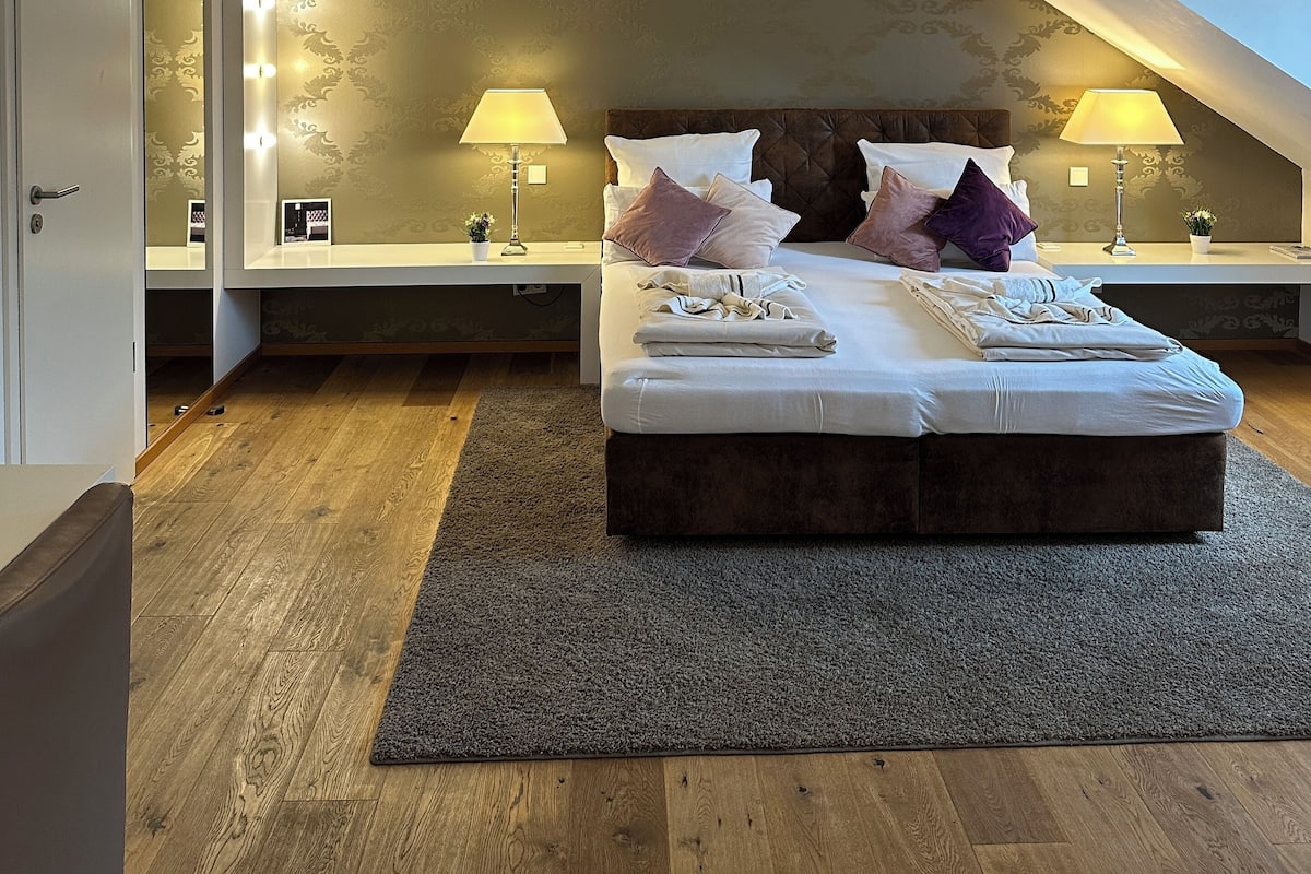 A modern bedroom with a large bed, two bedside tables with lamps, a mirror, and a ceiling fan.