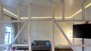 A modern interior with a wooden floor, a gray sofa, a white desk, and a TV. - Haven - Helvetia Suites Düsseldorf City (Düsseldorf)