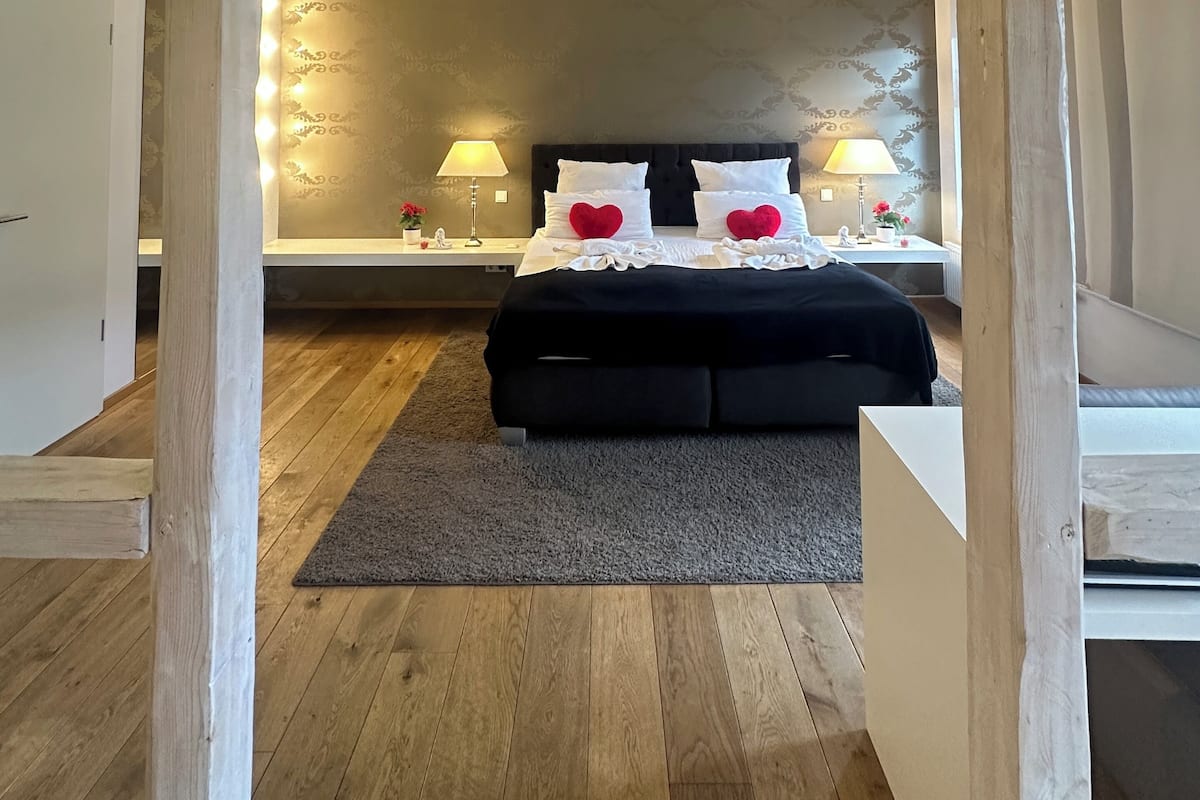 A bedroom with a bed, two bedside tables, a nightstand, a decorative wall, and a ceiling light fixture.