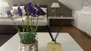 A bedroom with a bed, a bedside table with a lamp, a small potted plant, and a diffuser on a white table.