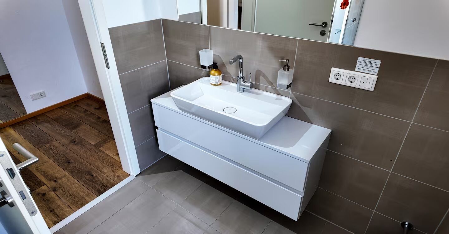 Ein modernes Badezimmer mit einem weißen Waschbecken, einem Spiegel und einem Handtuchhalter.
