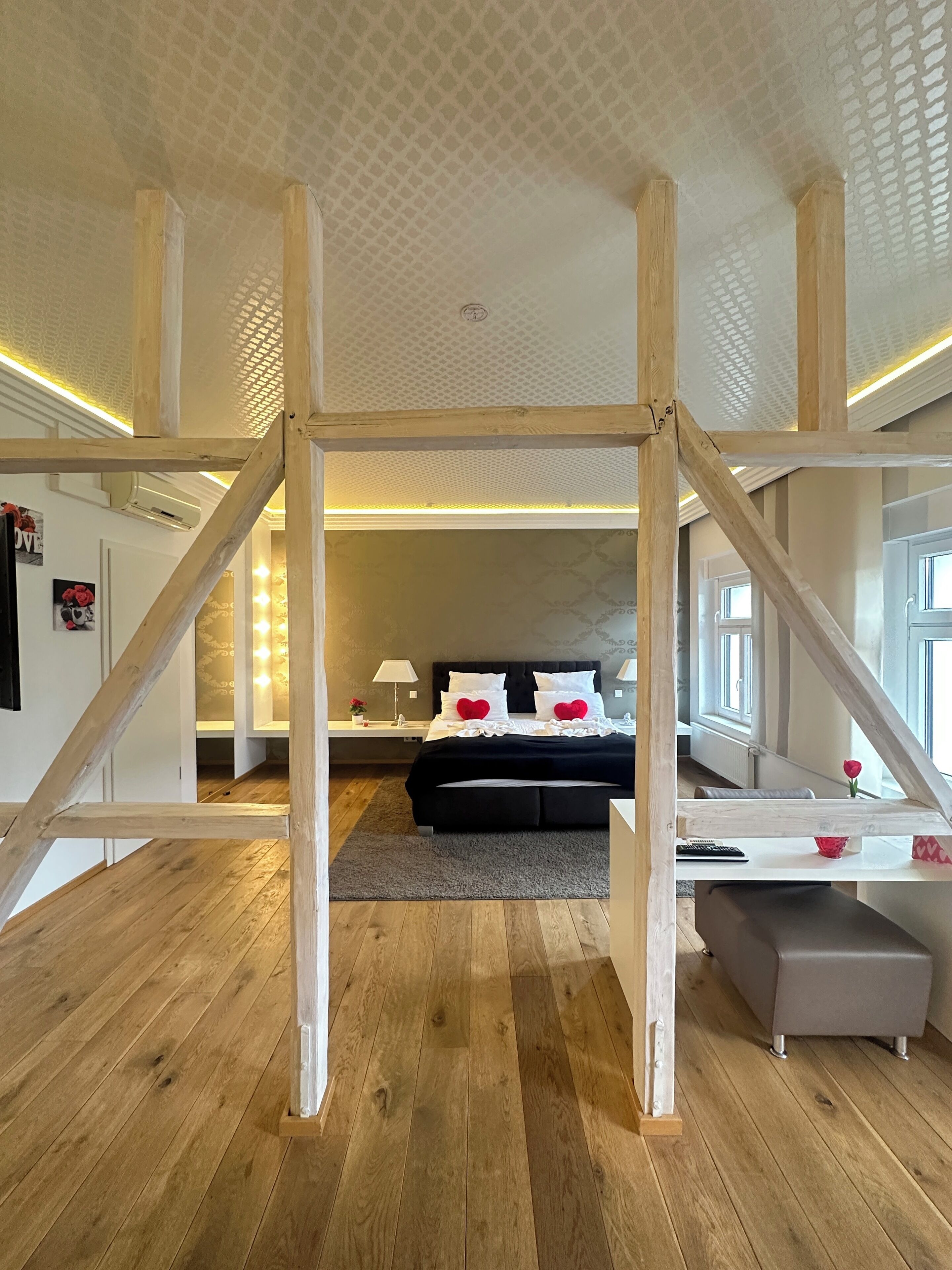Una camera da letto con travi a vista in legno, un letto con biancheria da letto bianca e cuscini rossi, un comodino con una lampada e una finestra con vista.