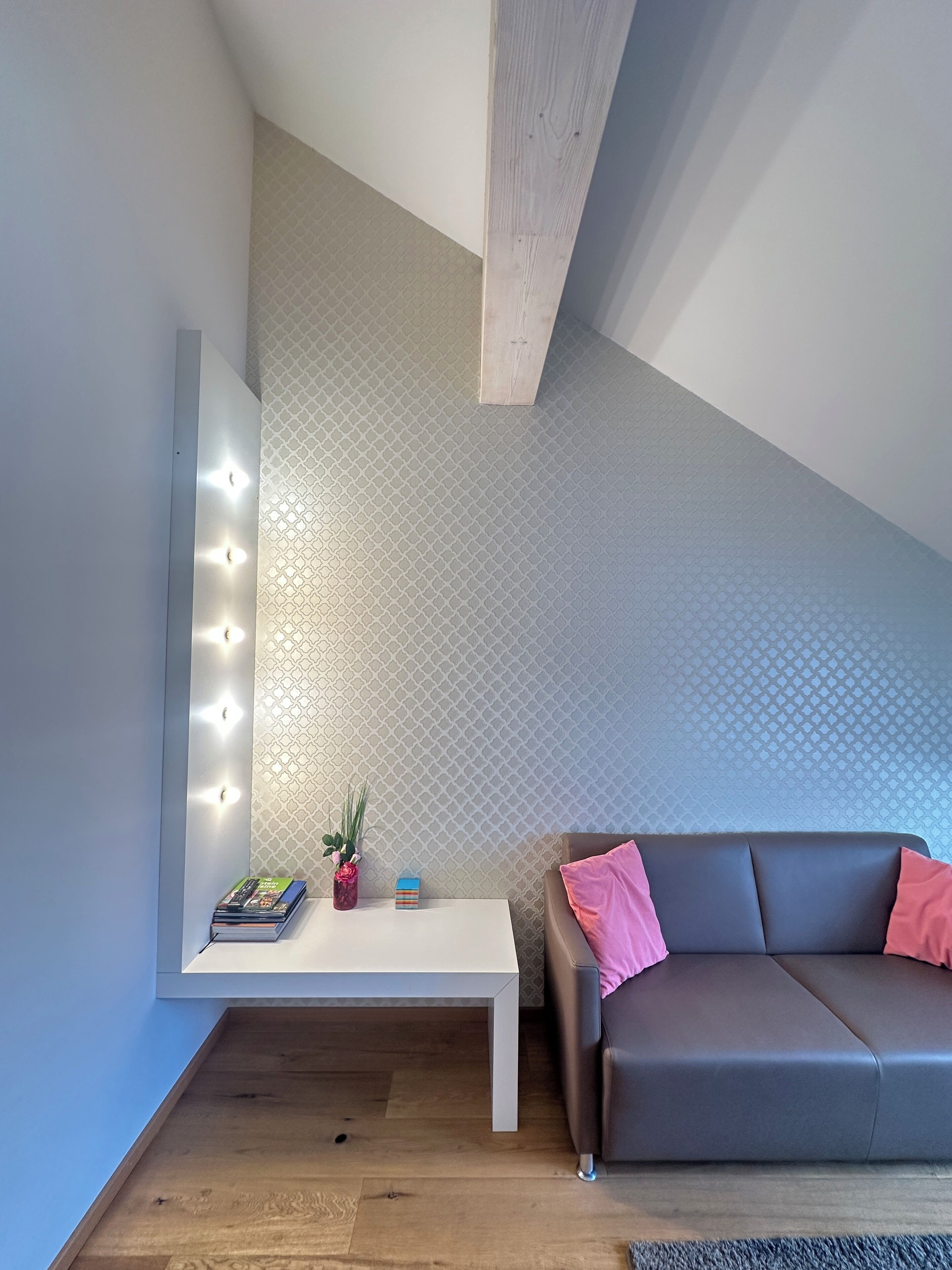 A modern living room with a white console table, a grey sofa, and a patterned wall.
