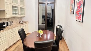 A dining area with a round table, four chairs, a chandelier, a kitchen with cabinets, and two framed artworks on the wall. - Haven - Helvetia Suites Düsseldorf City (Düsseldorf)
