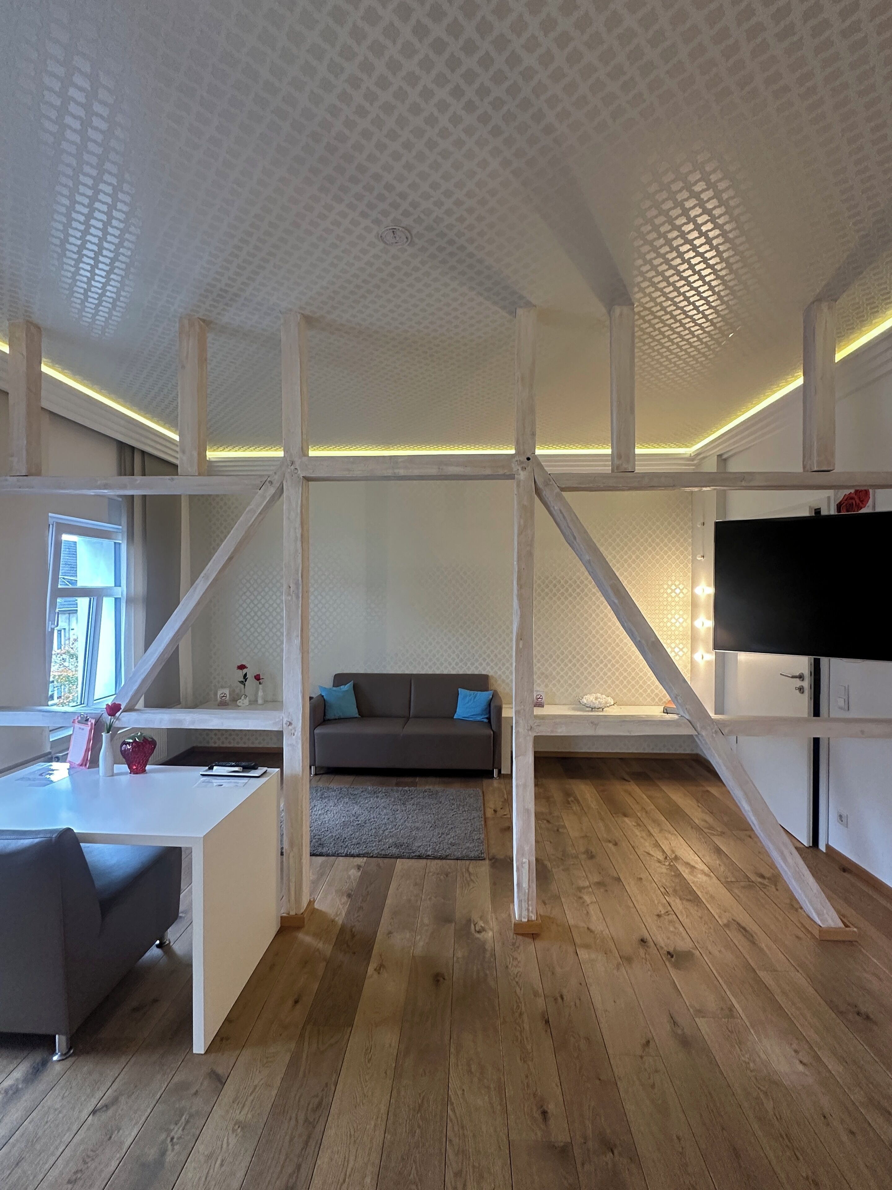Un interior moderno con suelo de madera, un sofá, un televisor y un escritorio blanco.