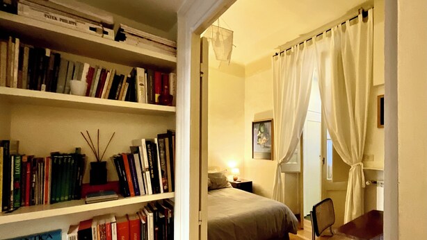 A bedroom with a bed, a chair, and a bookshelf filled with books. - Spanish Steps from my window (ROMA)