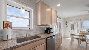 Una cocina con encimeras de granito, electrodomésticos de acero inoxidable, armarios de madera y un amplio ventanal que proporciona luz natural.