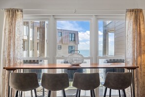 Un coin repas avec une table en bois et quatre chaises, un vase en verre décoratif, et une vue sur un bâtiment à travers de grandes fenêtres.