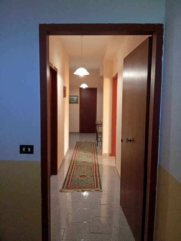 A hallway with a patterned carpet, a door on the right, and a light fixture above the door.