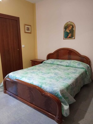 Une chambre à coucher avec un lit en bois, une table de chevet, une porte et un tableau encadré au mur.