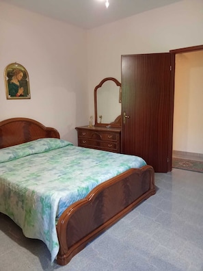 A bedroom with a wooden bed, a dresser, a mirror, and a door.