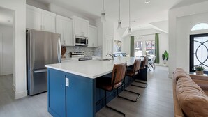 A modern kitchen with white cabinets, stainless steel appliances, a blue island, and a dining area with chairs. - Relax, Work, Play! Charming 3-bedroom house in amazing Dallas with Game Room (Dallas)