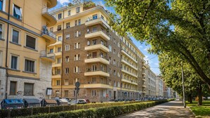 A multi-story residential building with balconies, a parking area, and a sidewalk lined with trees. - Casa Flaminia (Rome)