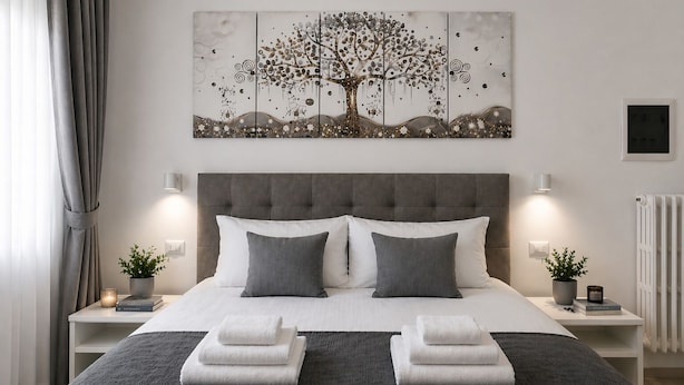 A modern bedroom with a large bed, grey and white bedding, two bedside tables with lamps, a wall-mounted artwork of a tree, and a radiator. - Casa Flaminia (Rome)