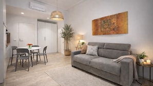 A modern living room with a grey sofa, a dining table with chairs, a hanging light fixture, and a large abstract painting on the wall. - Casa Flaminia (Rome)