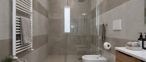 A modern bathroom with a glass-enclosed shower, a white toilet, a bidet, and a vanity with a sink.
