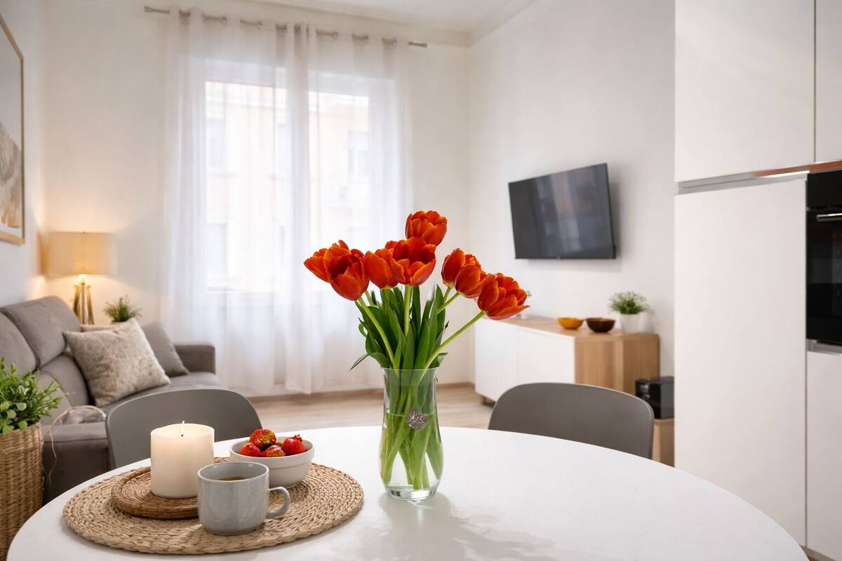 A modern living room with a white table, a vase of red tulips, a candle, and a bowl of strawberries.