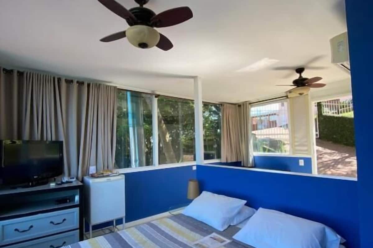 Ein Schlafzimmer mit Bett, Fernseher, Deckenventilator und großen Fenstern.